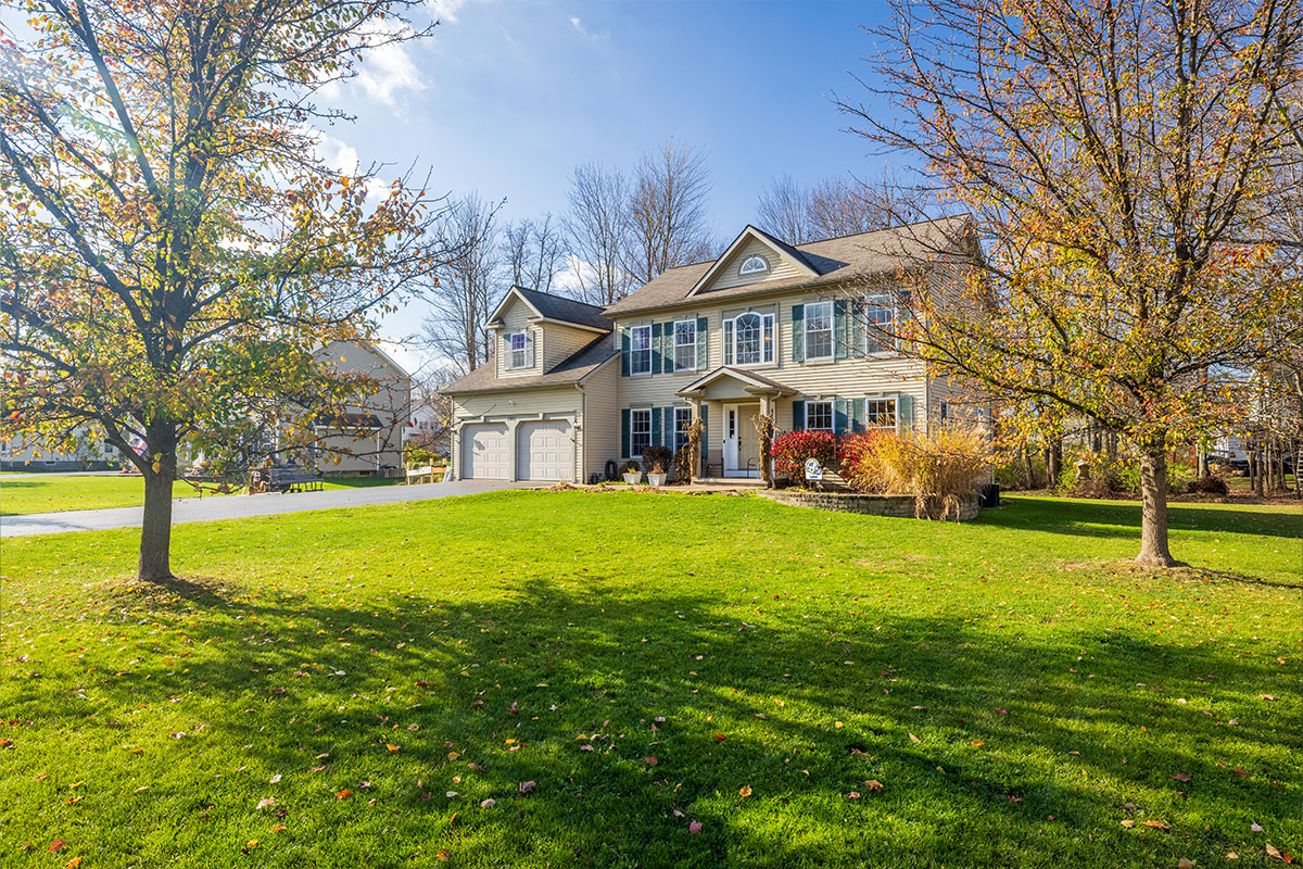 a colonial home with a large green lawn and trees