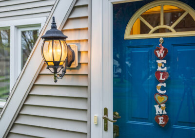 Warm porch light and blue front door with a “welcome” sign on a suburban home entry.
