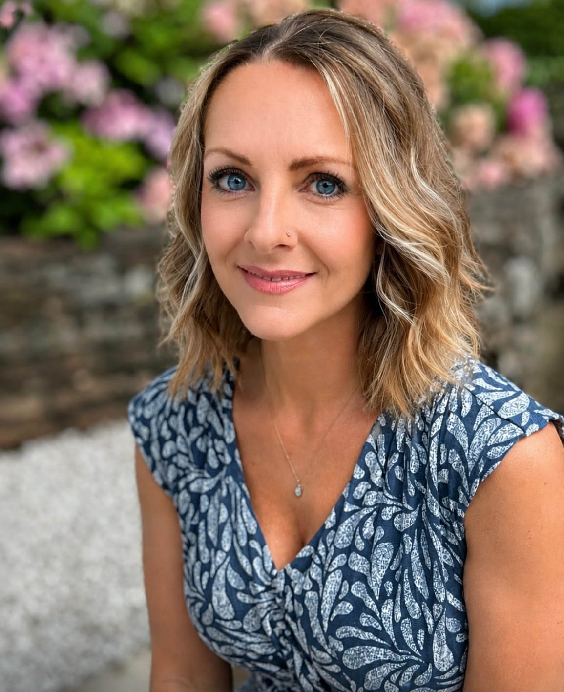 Headshot of hilary moore in a blue dress with a floral background