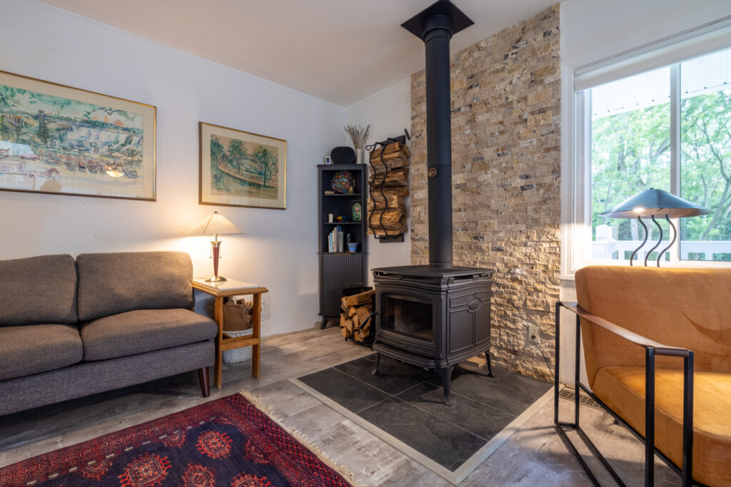 166 Moseley Rd, Fairport, NY 14450 4 Black wood-burning stove with a stone backdrop and adjacent firewood storage at 166 Moseley Road.