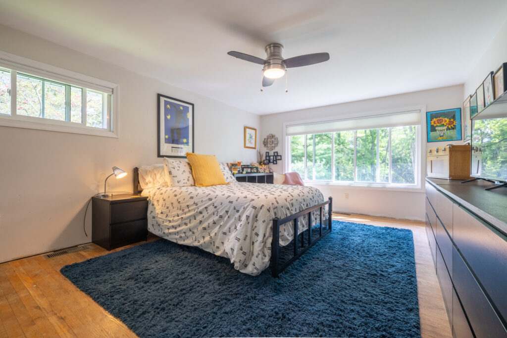 166 Moseley Rd, Fairport, NY 14450 6 Primary bedroom with a wide window overlooking trees and a ceiling fan at 166 Moseley Road.
