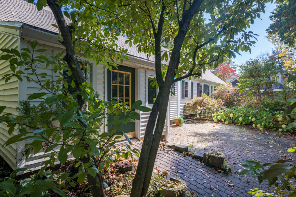 Shaded backyard brick-paver patio surrounded by mature trees and established gardens at 243 Overbrook Road in Pittsford NY